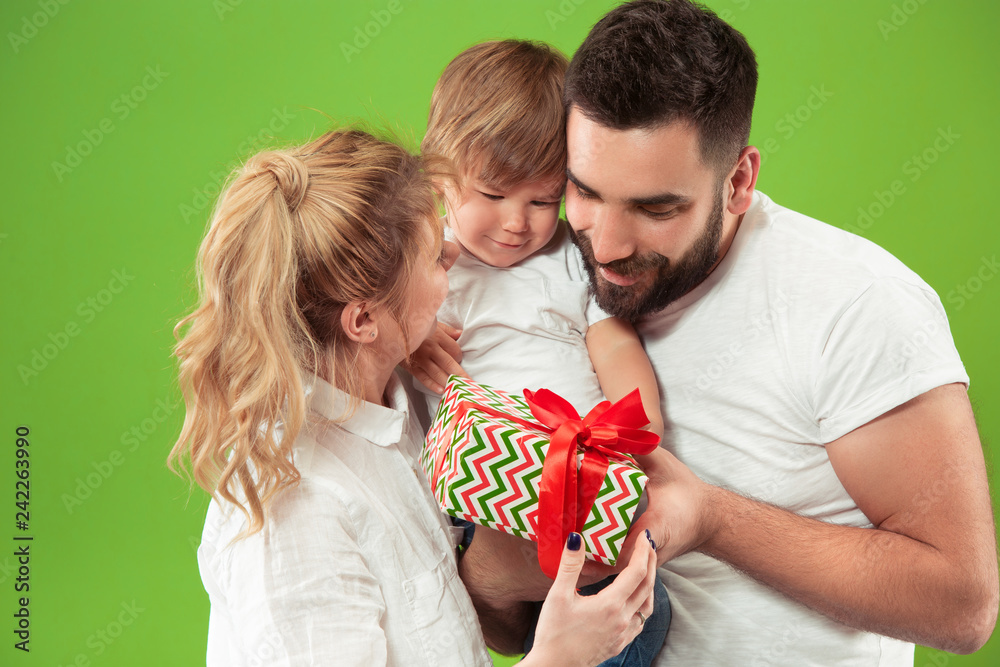 The happy family with kid posing together on green studio background. The people, togetherness, childhood, parent, love and lifestyle concept The happy family with kid posing together on green studio background. The people, togetherness, childhood, parent, love and lifestyle concept