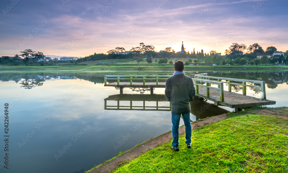 Man standing on a small bridge reflecting on the lake at sunrise as a relaxing way to welcome the beautiful new day