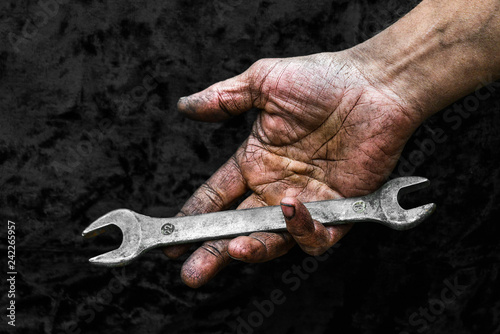 Dirty hand of working man with spanner wrench in car repair workshop photo