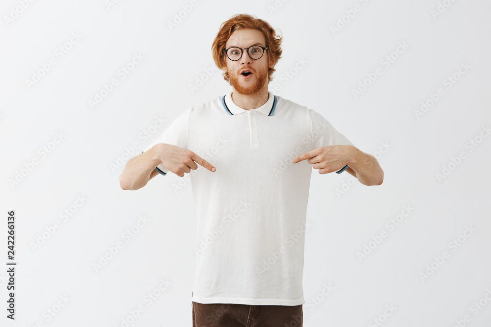 Look at my belly. Portrait of impressed and excited handsome redhead bearded young guy with messy hair pointing at chest or shirt with wow expression folding lips from amazement and surprise Look at my belly. Portrait of impressed and excited handsome redhead bearded young guy with messy hair pointing at chest or shirt with wow expression folding lips from amazement and surprise