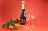 A bottle of champagne and two glass glasses. Next to the fir branch, Christmas-tree decoration and tangerines. Red background. Close-up. Free space under the text.