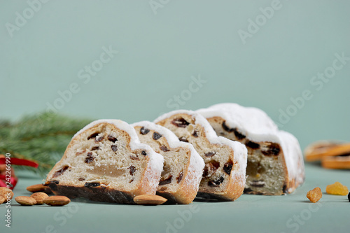 Slices of Christmas stollen. The frame space is occupied by slices of cake, cinnamon sticks, raisins and almond nuts. Light gray background. Close-up. Macro shooting. Free space under the text.