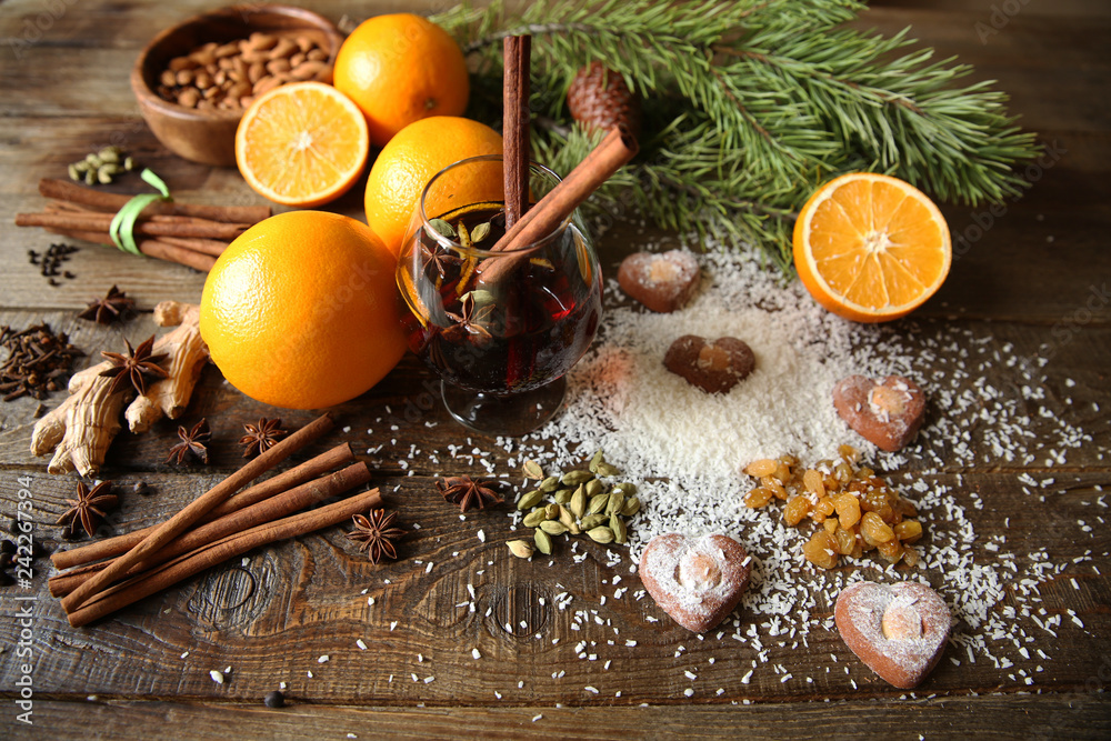 Christmas still life with mulled wine, heart-shaped cookies, coconut snow, nuts, oranges and spices on a wooden background with a fir branch