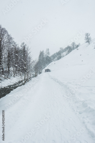 Verschneite Winterlandschaft mit Weg und Hütte an einem Bach