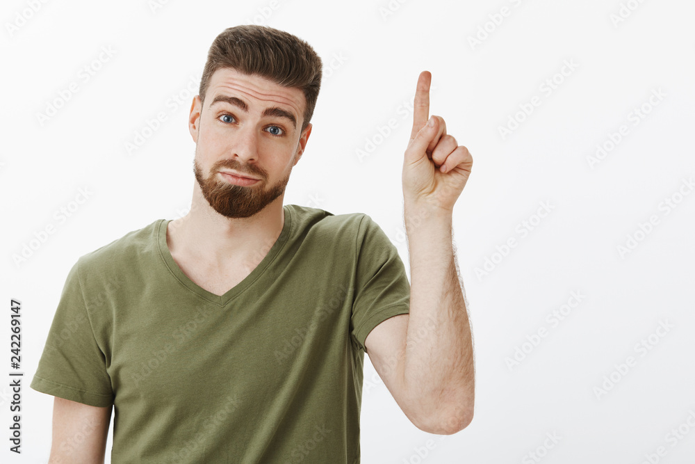 Guy have one suggestion raising index finger add idea standing silly and cute with hesitant and shy expression pouting tilting head and looking at camera with cute smile, pointing up over white wall Guy have one suggestion raising index finger add idea standing silly and cute with hesitant and shy expression pouting tilting head and looking at camera with cute smile, pointing up over white wall