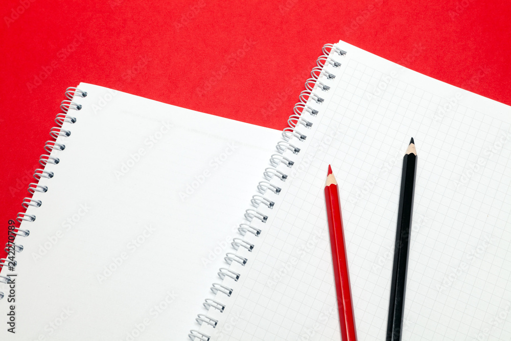 Notepad and red and black pensils blank sheets in cage white paper on spring on red background. Concept of free space, copyspace, business book, diary, use for notes at art seminar, conference Notepad and red and black pensils blank sheets in cage white paper on spring on red background. Concept of free space, copyspace, business book, diary, use for notes at art seminar, conference