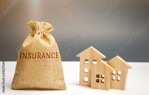A bag with money and the word Insurance and wooden houses. The concept of property insurance and housing. Accumulation of money for home insurance, health and life. Risks
