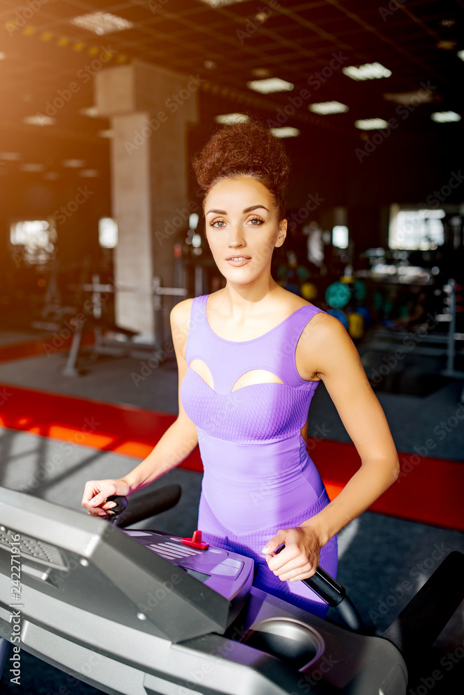 Sport world. Handsome woman in violet sportswear running in sports club on treadmill. Jogging her way to good health. Sport world. Handsome woman in violet sportswear running in sports club on treadmill. Jogging her way to good health.