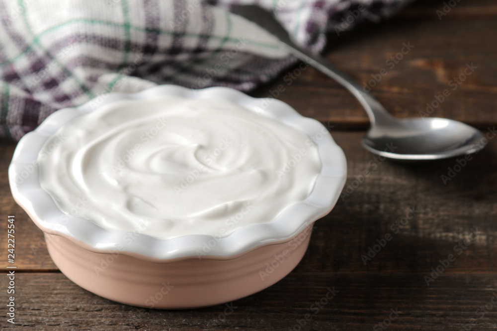 greek yogurt in a ceramic bowl next to a spoon on a brown wooden background greek yogurt in a ceramic bowl next to a spoon on a brown wooden background