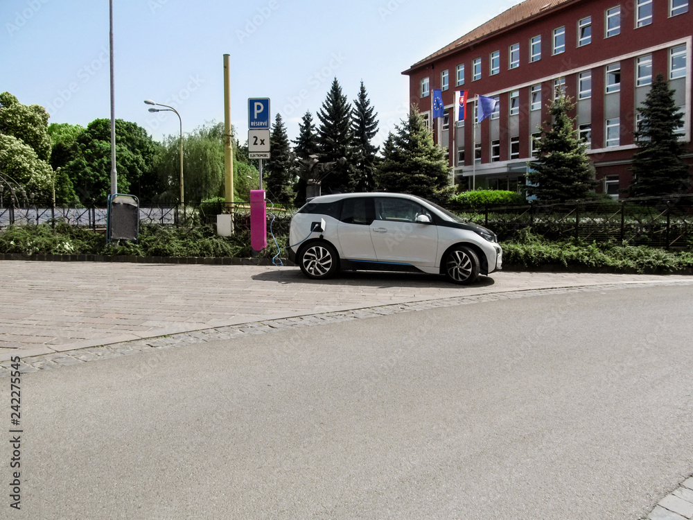 Modern white electric car charging on the street in Kosice, Slovakia. Summer cityscape with a car on an uncluttered clean street, picture with  copy space