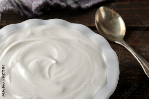 Greek yogurt in a ceramic bowl next to a spoon on a brown wooden background. close-up