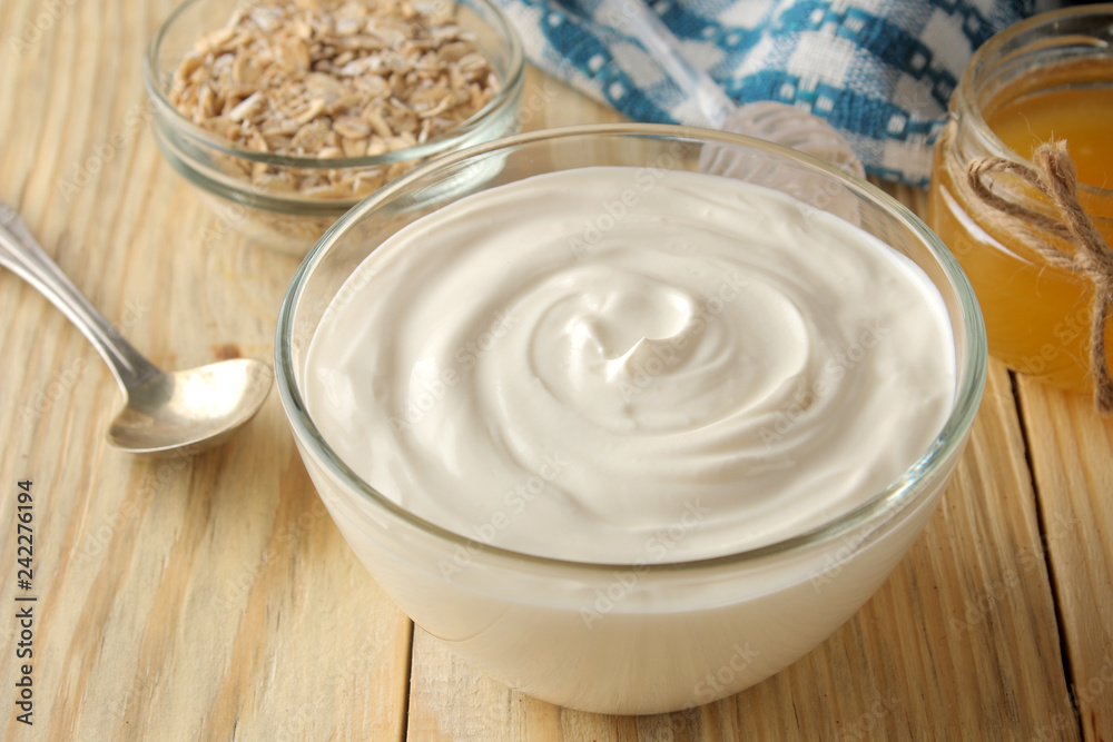 Greek yogurt in a glass bowl next to oatmeal and honey on a natural wood background. healthy food. natural yoghurt. breakfast. Greek yogurt in a glass bowl next to oatmeal and honey on a natural wood background. healthy food. natural yoghurt. breakfast.