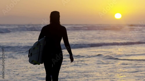 Surfer Carries Her Surfboard And Walks Along Shore, Waves Lap At Her Feet, Beautiful Sunset (Slow Motion)