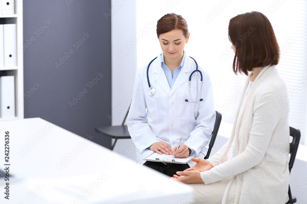Happy doctor and patient discussing something while sitting at the chairs at hospital. Physician at work in clinic. Medicine and healthcare concept Happy doctor and patient discussing something while sitting at the chairs at hospital. Physician at work in clinic. Medicine and healthcare concept