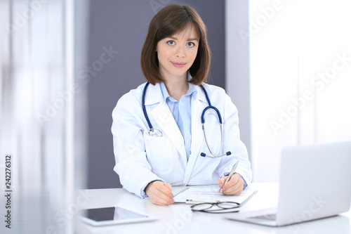Doctor woman at work. Female physician filling up medical form while sitting at the desk in clinic or hospital. Medicine and healthcare concept for advertising