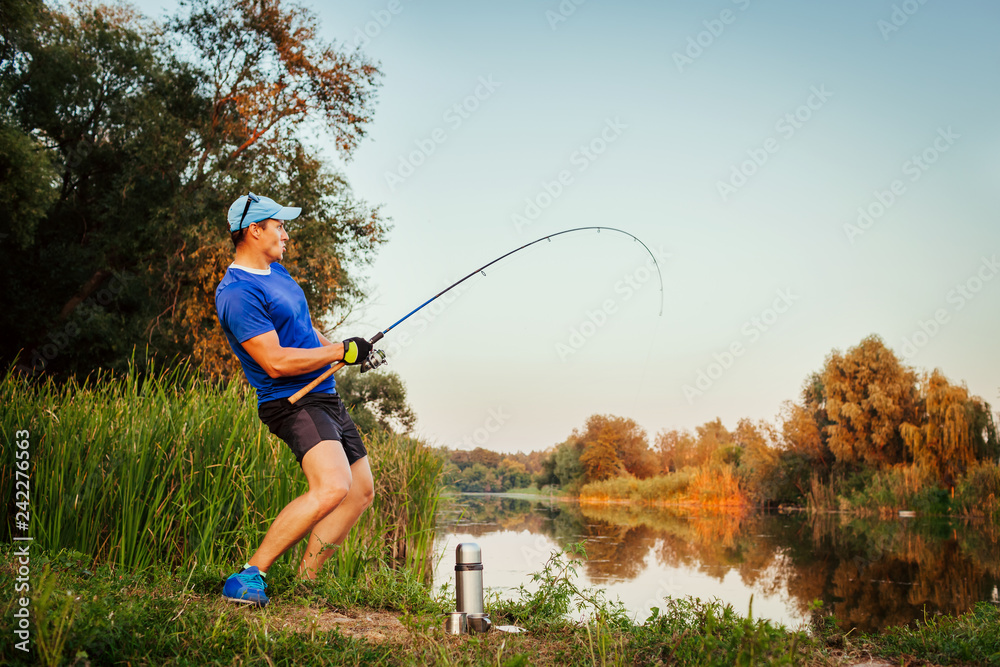 Young man fishing on river at sunset. Happy excited fiserman pulling rod  with fish. Stock Photo