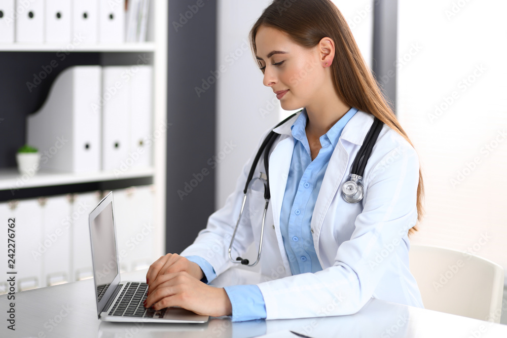 Doctor woman typing on laptop computer while sitting at the desk in hospital office. Physician at work. Medicine and health care concept