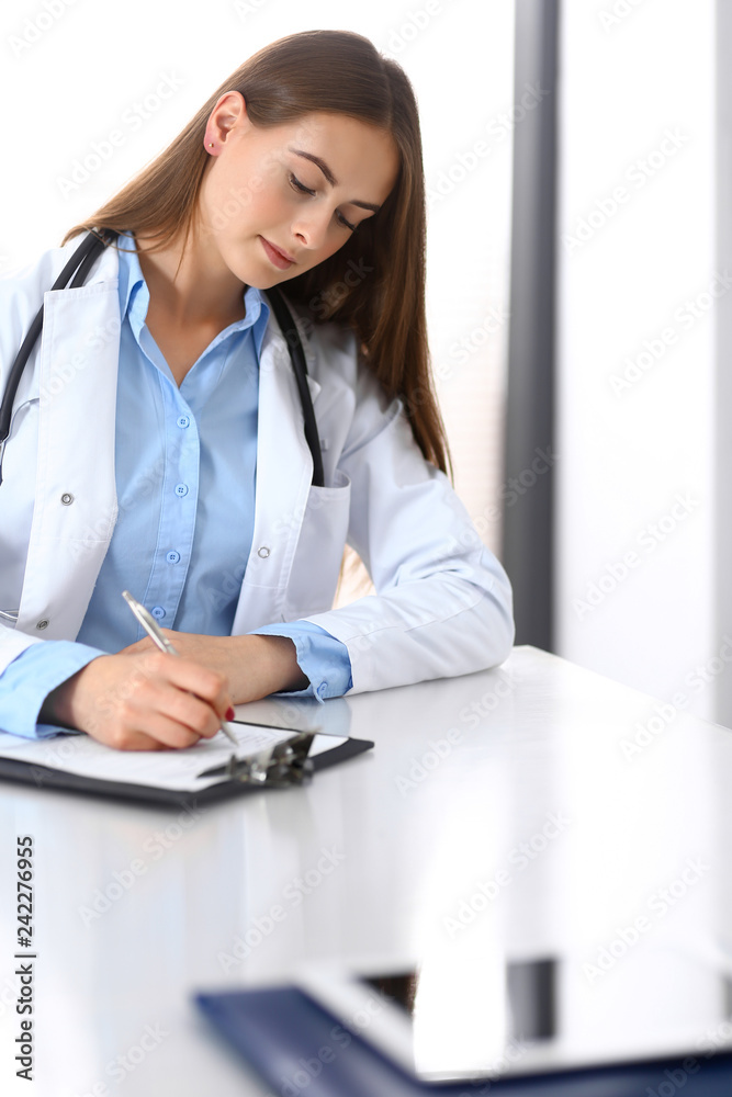 Doctor woman filling up medical form while sitting at the desk in hospital office. Physician at work. Medicine and health care concept Doctor woman filling up medical form while sitting at the desk in hospital office. Physician at work. Medicine and health care concept