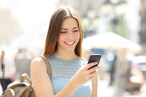Fotografia Happy girl walking in the street checking phone