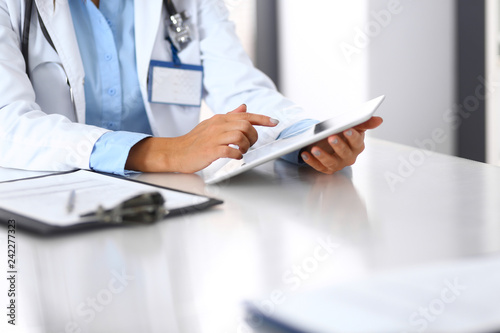 Unknown doctor woman using tablet computer while standing straight near window in hospital  close-up of hands. Medicine and health care concept