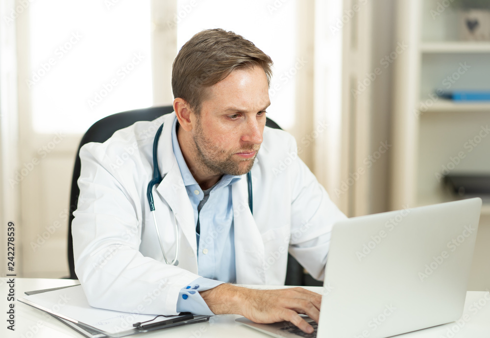 Handsome doctor working on medical expertise and searching information on laptop at hospital office Handsome doctor working on medical expertise and searching information on laptop at hospital office