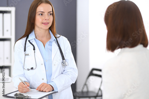 Doctor and patient discussing something while standing near reception desk in emergency hospital. Physician at work in clinic. Medicine and health care concept