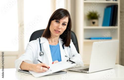 Female doctor working feeling up prescription and medical records with clipboard and laptop office