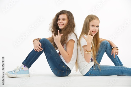 Two teen girl friends sit back to back on isolated white background.