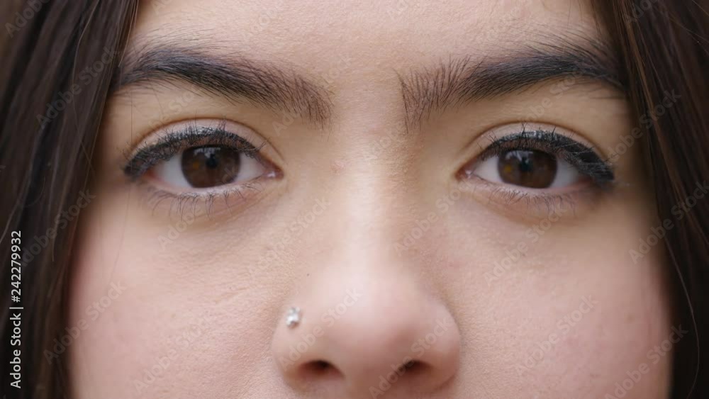 Dark brown eyes of young female open and look to camera 