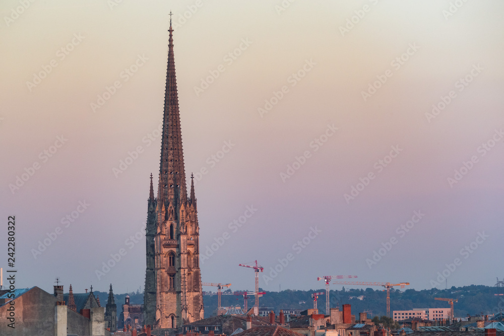 View of Basilica of St. Michael steeple tower with construction cranes in the background at sunset, city of Bordeaux, France View of Basilica of St. Michael steeple tower with construction cranes in the background at sunset, city of Bordeaux, France