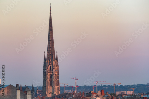 View of Basilica of St. Michael steeple tower with construction cranes in the background at sunset, city of Bordeaux, France