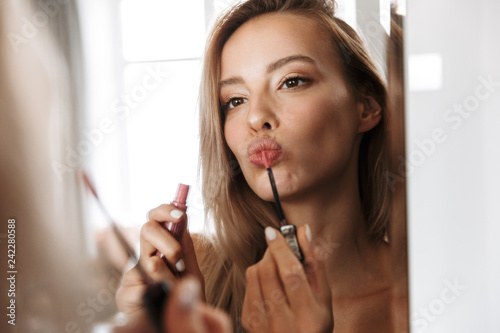 Young woman in lingerie underwear looking at mirror apply her lipstick lip gloss doing makeup.