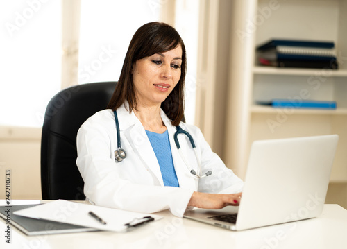Female doctor working with stethoscope and clipboard in medical office with natural face expression