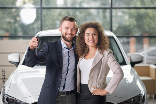 Happy couple posing with new white car and keys.