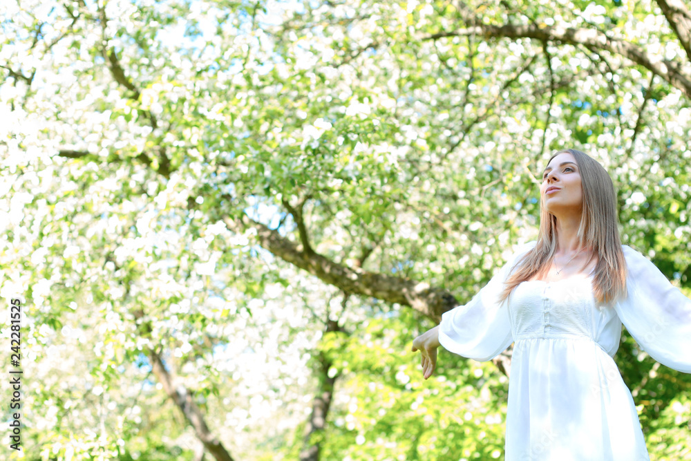 Happy blonde woman on a background of blooming spring garden with her hands raised to the sky Happy blonde woman on a background of blooming spring garden with her hands raised to the sky