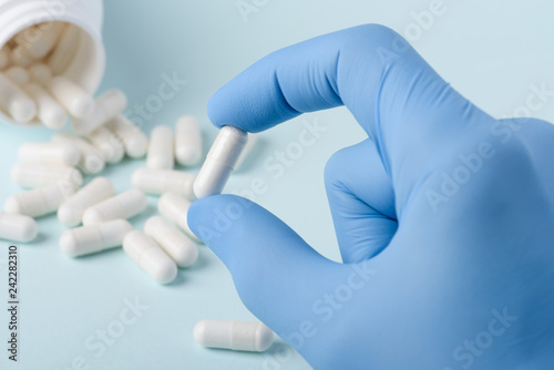 Single pill with white substance in scientist hand, bottle on background