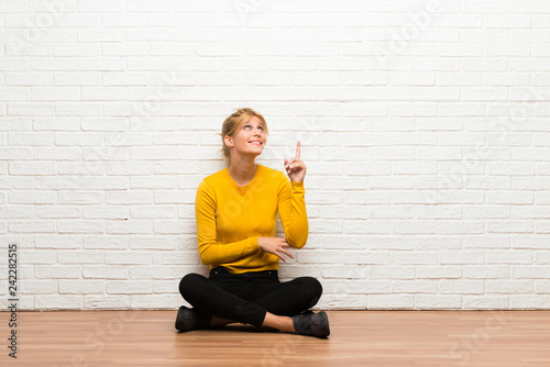 Young girl sitting on the floor pointing a great idea and looking up