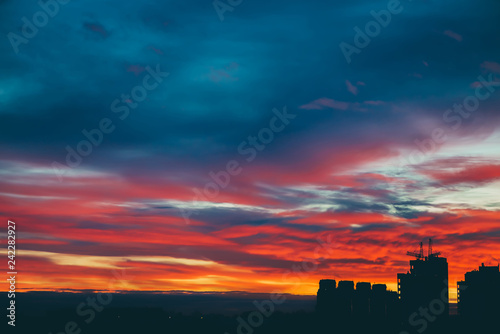 Cityscape with wonderful varicolored vivid dawn. Amazing dramatic multicolored cloudy sky above dark silhouettes of city buildings. Atmospheric background of sunrise in overcast weather. Copy space.