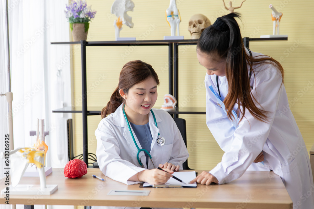 Two female doctors with stethoscope in white overalls doing paperwork in office together. Two female doctors with stethoscope in white overalls doing paperwork in office together.