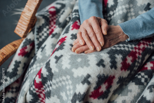 partial view of senior woman sitting in wicker rocking chair with blanket and folded hands at home