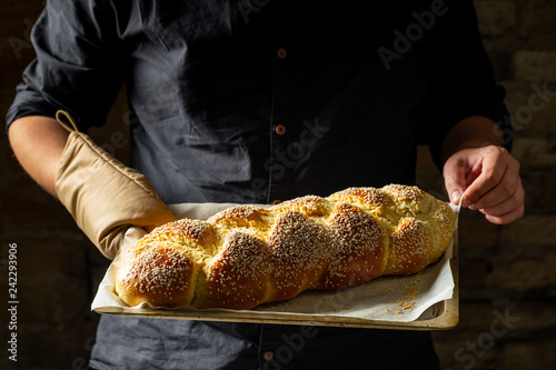Baker holding baking tray with fresh baked challah jewish bread
