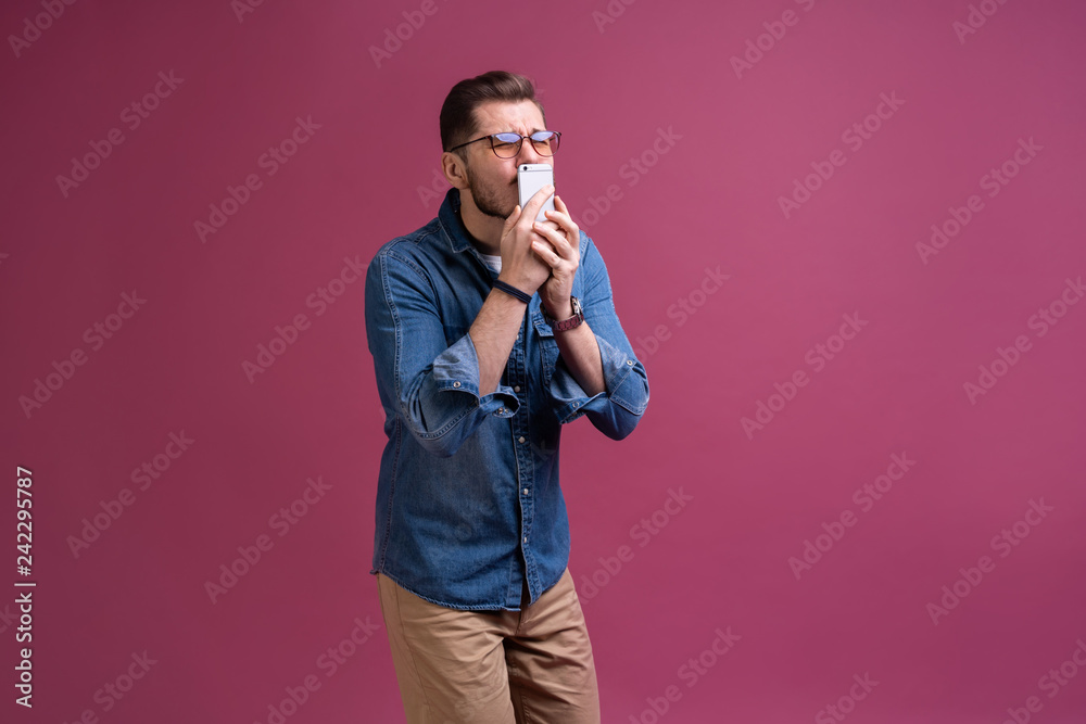 Always in touch. Smiling young man holding smart phone and looking at it. Portrait of a happy man using mobile phone isolated over pink background Always in touch. Smiling young man holding smart phone and looking at it. Portrait of a happy man using mobile phone isolated over pink background