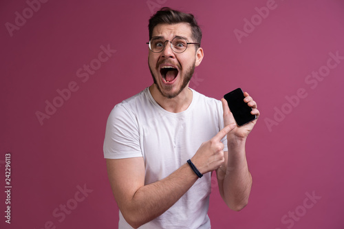 You will have problems man! Portrait of angry confused aggressive in bad mood guy shouting threatening in the loud-speaker of his smartphone, isolated on pink background.