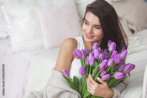Close up portrait of young beautiful woman indoors. Attractive woman with flowers. Female with tulips. Spring bouquet.