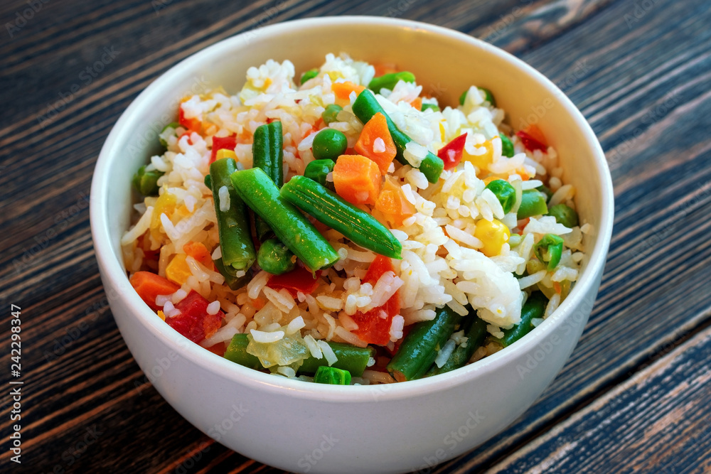 A Cup of white rice with vegetables on a dark wooden background. Prepared without loss of vitamins. A Cup of white rice with vegetables on a dark wooden background. Prepared without loss of vitamins.