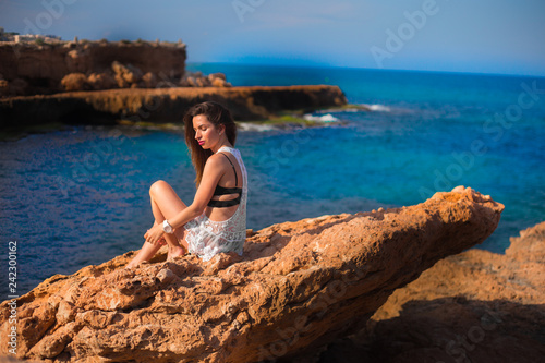 Model sitting on edge of rocks with sea view 