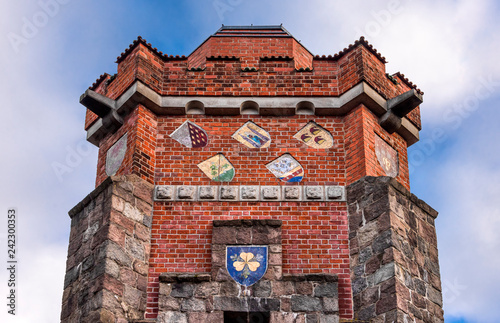 Germany, Pritzwalk, Trappenberg: Historic Bismarck tower (Bismarckturm) from below with brick exterior wall, window, old crests, battlement, observation deck and blue cloudy sky - concept monument