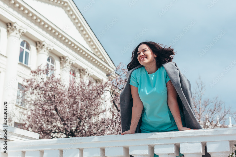 Beautiful model in blue dress and grey coat by spring blooming tree