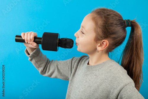 Kid girl sings into a microphone on a yellow background.