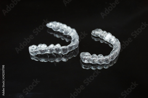 A pair of upper and lower clear retainers or aligners side by side on a dark reflective surface against a black background.